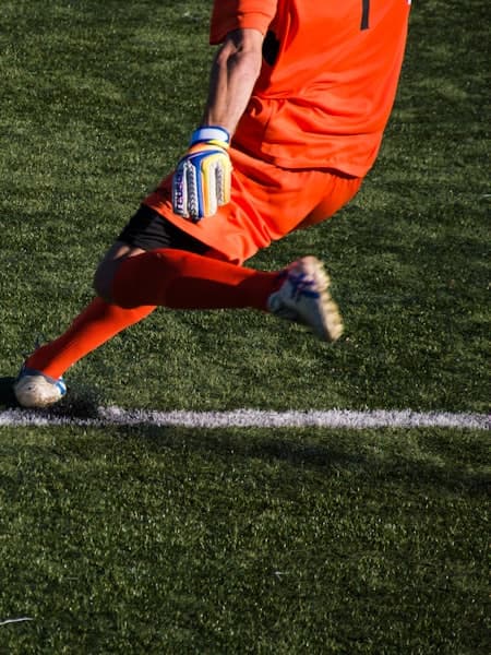 Goalkeeper in orange stretching for the ball