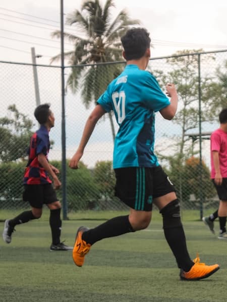 Youth players sprinting on a pitch lined with palm trees
