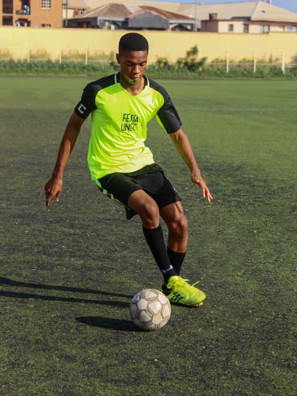 Player in a neon green kit dribbling on a grass pitch